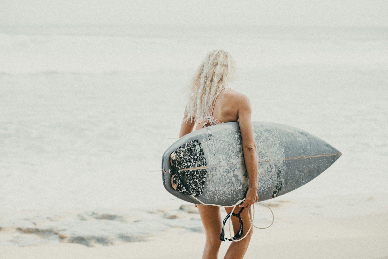 A woman standing on a beach holding a surfboard